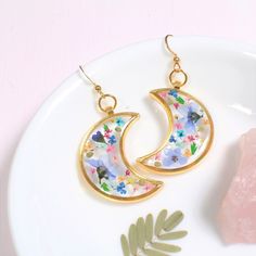 a pair of earrings sitting on top of a white plate next to a pink rock