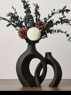 two black vases with flowers in them on a table