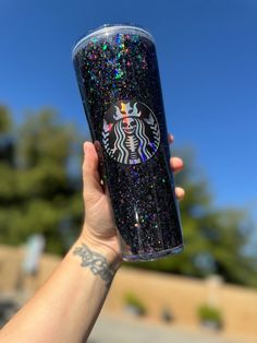 a person holding up a starbucks cup with glitter on the lid and bottom, in front of a blue sky