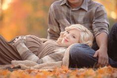 a man and woman laying on the ground with leaves all around them in front of trees