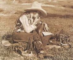 an old photo of a man wearing a cowboy hat sitting in the grass with his horse