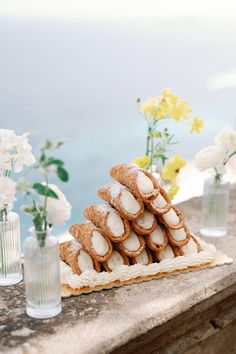 a table topped with cookies and flowers next to vases filled with white flowers on top of a stone wall