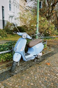 a blue scooter parked next to a street light on a cobblestone road