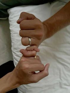 two people holding hands while sitting on top of a bed in front of white pillows