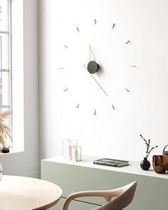 a clock on the wall next to a table and chair in a room with white walls