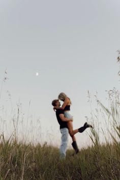 a man and woman standing in tall grass with their arms around each other as they hug