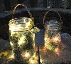 two mason jars with fairy lights in them sitting on a stone patio area next to a fire pit