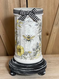 a white vase with yellow flowers and a black ribbon around the top is sitting on a wooden table