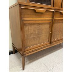 a wooden cabinet with wicker doors and drawers on the bottom shelf, next to a tiled floor