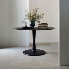 a black table with books and vases on it in front of a white wall