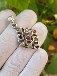 a hand holding a silver pendant with different colored stones