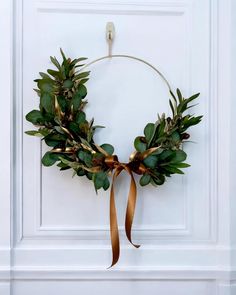 a wreath hanging on the front door with gold ribbon and greenery around it's edges