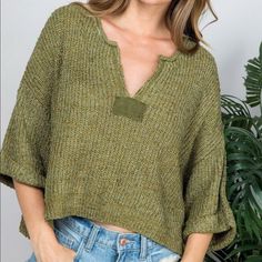 a woman wearing a green sweater with a pocket on her left shoulder and jeans on the right