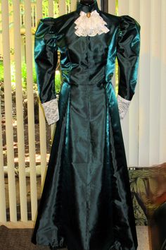 **YOU MUST TAKE YOUR MEASUREMENTS PRIOR TO CHOOSING A SIZE** This Edwardian/Victorian dress is actually a top and skirt, made in a beautiful bridal taffeta.  The photos display it in an emerald green color, but I am able to make it in any color you choose. The top is fully lined and lightly boned.  The puffed upper sleeves are stiffened with interfacing, and the lower sleeves are embellished with lace.  A lace-layered stay accompanied by a faux cameo pin at the neckband completes the look.  The top has hook and eye closures down the front of the bodice. The full length skirt is delicately pleated at the center back and also has hook and eye closures.  The hem is stitched by hand, and any exposed seams are overcast.  BODY MEASUREMENTS for Teens/Adults sizes are approximately: Size 6 - Chest Fitted Long Sleeve Dresses For Cosplay, Fitted Victorian Floor-length Dress For Costume Parties, Fitted Floor-length Victorian Dress For Costume Party, Fitted Floor-length Victorian Costume Dress, Green Formal Dress With Historical Design, Formal Green Dress With Historical Design, Vintage Fitted Dress For Cosplay Events, Elegant Fitted Formal Costumes, Victorian Fitted Costume For Fancy Dress