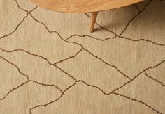 an area rug with brown lines on it and a wooden table in the corner next to it