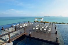 an outdoor wedding set up with white chairs on the dock overlooking the ocean and blue sky