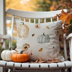 a white chair with two pumpkins on it and a pillow sitting on top of it