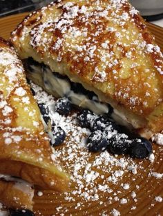 two pastries on a plate covered in powdered sugar and blueberry toppings