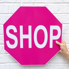 a person holding up a pink sign with the word shop written in white on it