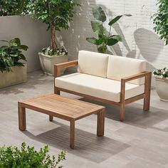 a wooden bench sitting next to a white couch on top of a cement floor near potted plants