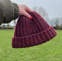 a hand holding a red knitted hat on top of a green field