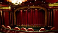 an empty theater with red curtains and chairs in it's center stage, as well as chandeliers