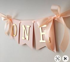 a pink banner with the word one hanging from it's side and ribbon on top