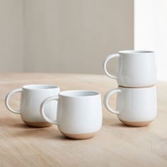 three white cups sitting on top of a wooden table