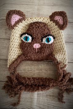 a crocheted bear hat with blue eyes on top of a wooden floor,