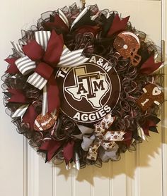 the texas a & m aggies wreath is hanging on a door with red and white ribbons