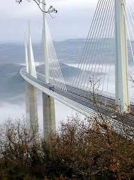 a very tall bridge over some water on a cloudy day with fog in the air