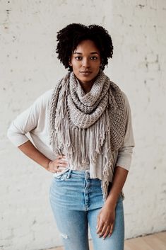 a woman standing in front of a white wall wearing a scarf and jeans with her hands on her hips