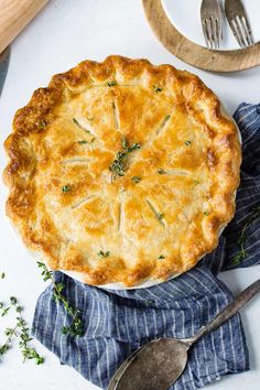 a pie sitting on top of a blue cloth next to a knife and spoons