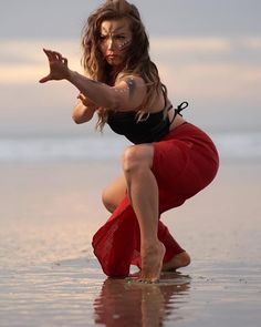 a woman in a black top and red skirt on the beach with her arms outstretched