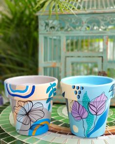 two flower pots sitting on top of a table next to each other with flowers painted on them