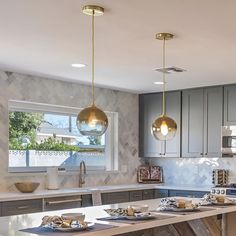 a kitchen with marble counter tops and gold pendant lights hanging from the ceiling over the island