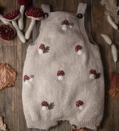 a knitted baby romper with mushrooms and leaves on the ground next to it