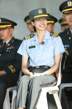 a woman in uniform is sitting on a chair and smiling at the camera while other uniformed men are behind her