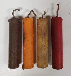 four different colored candles lined up next to each other on a white surface with one red, one orange and one brown