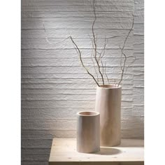 two white vases sitting on top of a wooden table next to a brick wall