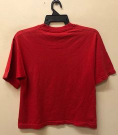 a red t - shirt hanging on a hanger in front of a white wall