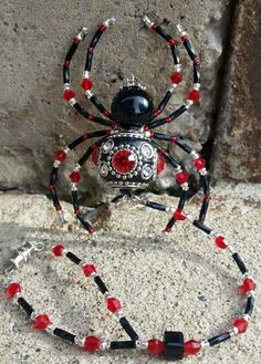 a red and black beaded spider necklace on a stone wall next to a chain