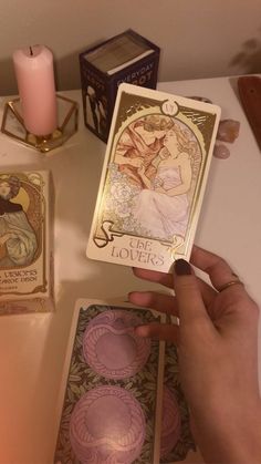 a person holding up a tarot card next to some other cards on a table