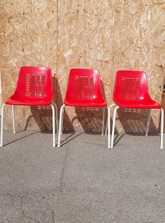 three red chairs sitting next to each other in front of a wall