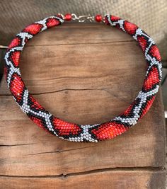 a red and black beaded necklace sitting on top of a wooden table