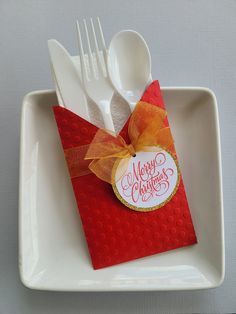 a white plate topped with a red and orange christmas card next to plastic utensils