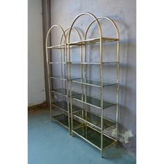 a gold metal shelf with glass shelves on the top and bottom, against a gray wall