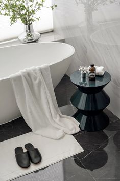 a pair of black slippers sitting on top of a table next to a bath tub