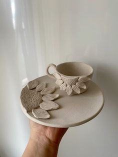 a hand holding a white plate with flowers on it and a cup in the middle