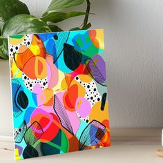 a colorful abstract painting on a white table next to a potted plant and clock